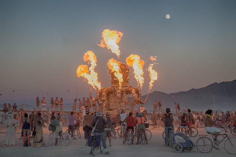 An art installation on fire at the Burning Man Festival while a crowd of people watch